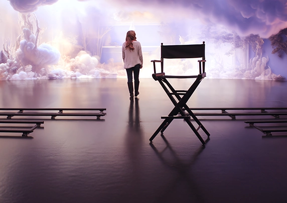 A woman facing away from the camera walks from a director's chair and toward an AI-generated cloud backdrop on a film set.